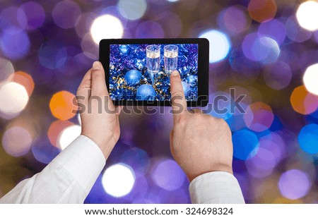 man takes photo of Christmas still life - two glasses of champagne in blue Xmas balls and tinsel on blured violet Christmas tree light bokeh background