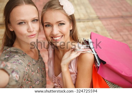 Two girls with shopping bags are taking pictures of themselves. High angle view. Shoot looks like selfie