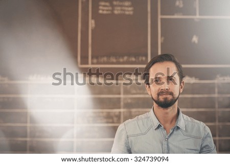 Handsome designer businessman standing in his workshop in front of a chalk board, looking confidently at the camera