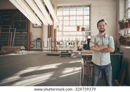 Portrait of a good looking male designer standing in his workshop studio with his arms folded and smiling confidently at the camera Royalty-Free Stock Photo #324739379