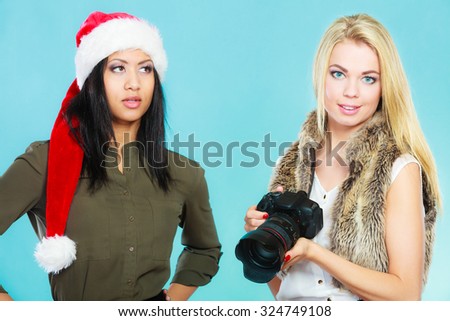 Photographer and model. Caucasian blonde girl shooting images, taking photos with camera., photographing african woman in santa helper hat.