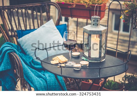 Beautiful terrace or balcony with cozy rattan armchair and wine glass on small iron table. Toned picture