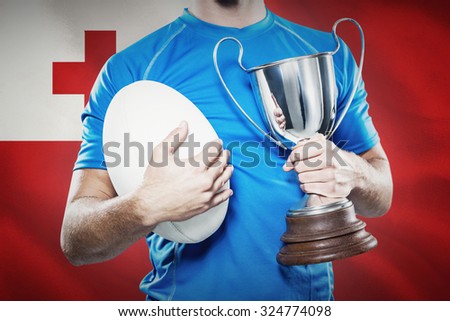 Rugby player holding trophy and ball against close-up of tongan flag