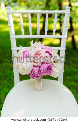 Beauty of colored flowers. Bridal accessories. Close-up bunch of florets. Details for marriage and for married couple. Wedding bouquet with peonies, roses and orchids on the white chair