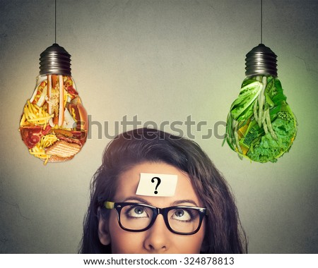 Woman in glasses question mark on head thinking looking up at junk food and green vegetables shaped as light bulb isolated on gray background. Diet choice right nutrition healthy lifestyle concept   Royalty-Free Stock Photo #324878813