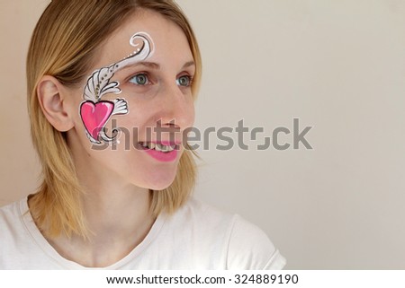 Smiling young blond woman with her face painted with pink heart