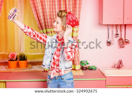 Pretty pin-up girl teenager taking picture of herself on a pink kitchen. Beauty, youth fashion. Pin-up style. Selfie.