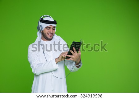 Emirati man using digital tablet and listening music on headphones