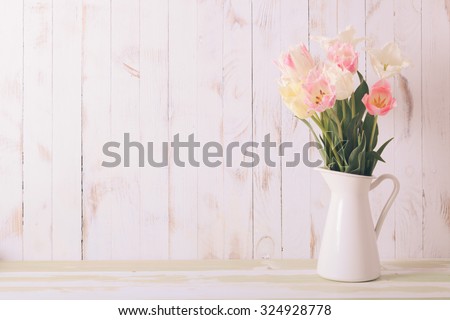 White vase with delicate shades armful of tulips on a wooden background