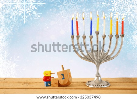 image of jewish holiday Hanukkah with menorah (traditional Candelabra) and wooden dreidels (spinning top). glitter and snowflakes overlay 
