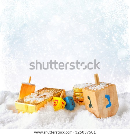 image of jewish holiday Hanukkah with wooden colorful dreidels (spinning top) over december snow with glitter and snowflake background 