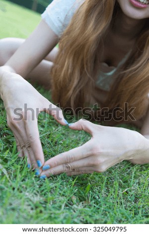 asia woman sitting on grass making heart with her fingers