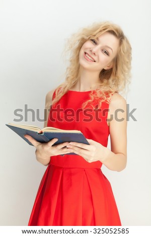 Beautiful blonde in a red dress with a book on a gray background.