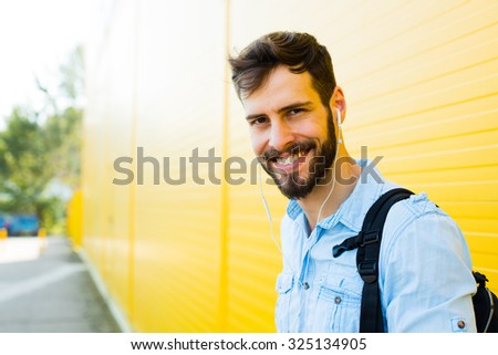 handsome student with backpack outside on yellow background