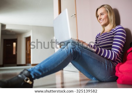 Female student sitting on flooring using laptop in college