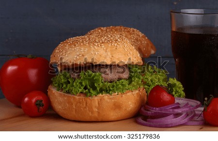 Big tasty appetizing fresh burger of green lettuce cheese bacon slice meat cutlet and white bread bun with sesame seeds and potato chips on wooden table and cola, horizontal picture