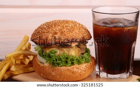 Big tasty appetizing fresh burger of green lettuce red tomato cheese and bacon slice meat cutlet and white bread bun with sesame seeds and glass of cola, horizontal picture