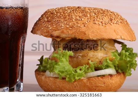 Big tasty appetizing fresh burger of green lettuce red tomato cheese and bacon slice meat cutlet and white bread bun with sesame seeds and glass of cola, horizontal picture