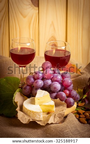 Red wine with cheese, almonds and grapes on sackcloth on a background of a wooden wall and autumn leaves. For this photo applied vignetting effect.