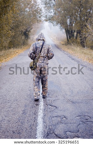 Picture of man in camouflage running on empty autumn countryside road. Backview of soldier in hood on foggy cold outdoor background.