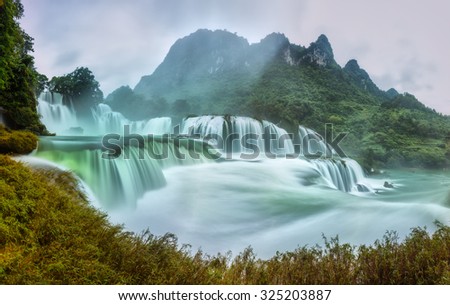 Ban Gioc Waterfall craggy limestone permissive side misty morning with foreground grass and tones of the lower cascade. It is considered the most beautiful waterfalls Asia.