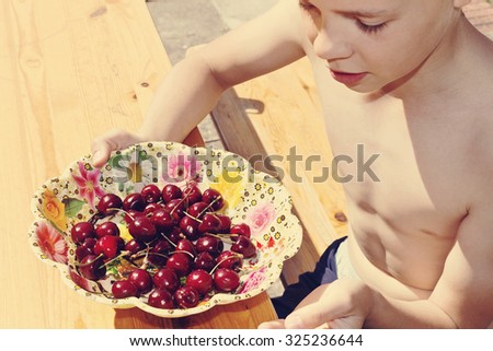 boy holding a bowl of ripe a sweet cherry. selective focus. image is tinted