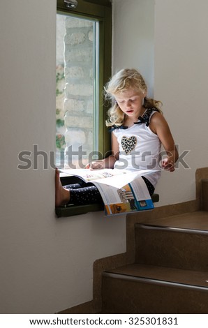beautiful scholar blond girl sitting by the window and reading book