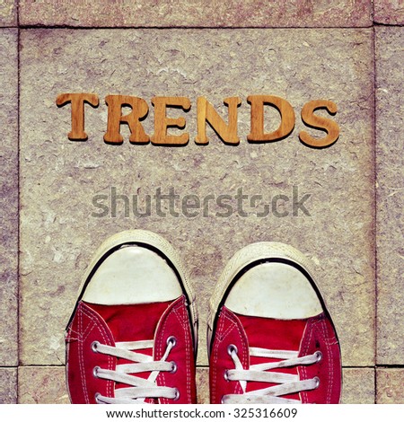 high-angle shot of some wooden letters forming the word trends and the feet of a man wearing red sneakers on the street
