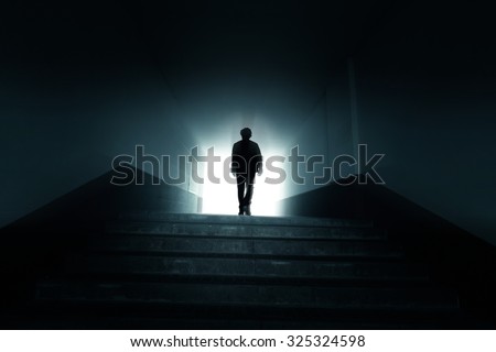 Man walking to the light in the dark tunnel. Royalty-Free Stock Photo #325324598