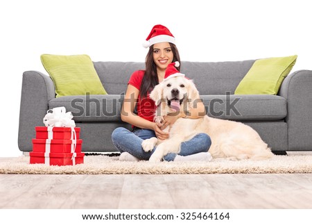 Young woman with Santa hat sitting on the floor in front of a gray couch and hugging her pet dog isolated on white background