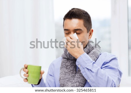 healthcare, flu, people, rhinitis and medicine concept - ill man blowing his nose with paper napkin and drinking tea at home Royalty-Free Stock Photo #325465811