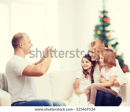 family, holidays, technology and people - smiling mother, father and little girls with camera over living room and christmas tree background