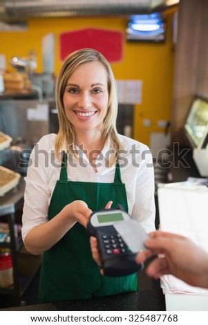 Portrait of female worker accepting payment from customer through credit card in bakery
