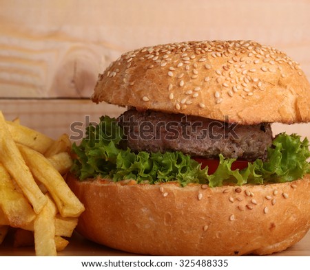 One big tasty appetizing fresh burger of green lettuce red tomato cheese and bacon slice meat cutlet and white bread bun with sesame seeds and potato chips, horizontal picture