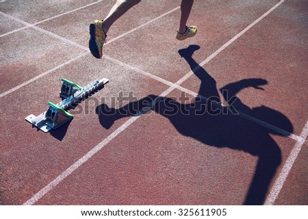 Athlete in gold shoes sprinting from the starting blocks over the starting line of a race on a red running track 