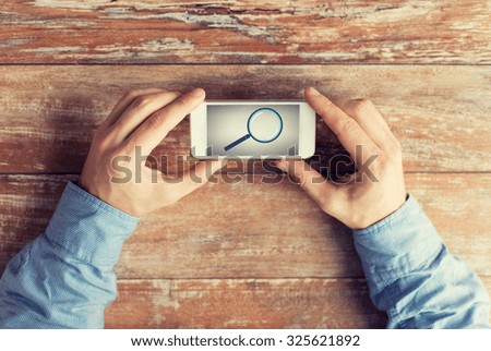 business, education, people and technology concept - close up of male hands holding smartphone with magnifying glass picture on screen at table