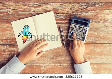 business, education, people and technology concept - close up of female hands with calculator, pen and rocket drawing in notebook on table