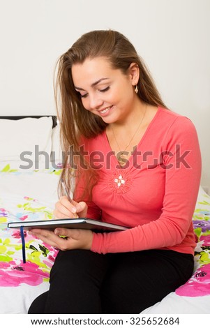 young woman writing sitting on her bed