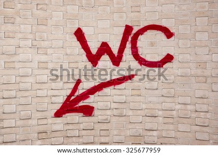 Graffiti Art Urban Street Handmade Red Sign WC With Arrow On The White Brick Wall Background