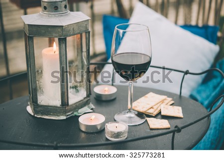 Glass of wine and candles on small iron table on the terrace or balcony. Toned picture
