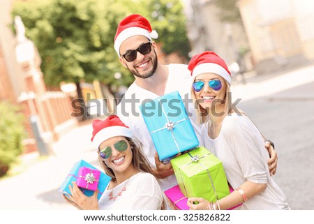 A picture of group of friends in Santa's hats sitting in the city with presents
