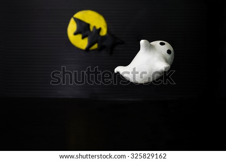 Halloween cute ghost with black bat in front of the bright yellow full moon against black background