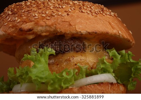 One big tasty appetizing fresh burger of green lettuce red tomato cheese and bacon slice meat cutlet and white bread bun with sesame seeds closeup, horizontal picture