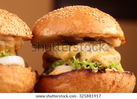 Big tasty appetizing fresh burgers of green lettuce red tomato cheese and bacon slice meat cutlet and white bread bun with sesame seeds closeup, horizontal picture