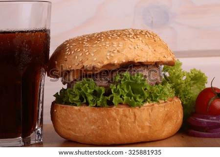 Big tasty appetizing fresh burger of green lettuce cheese bacon slice meat cutlet and white bread bun with sesame seeds and potato chips on wooden table and cola, horizontal picture