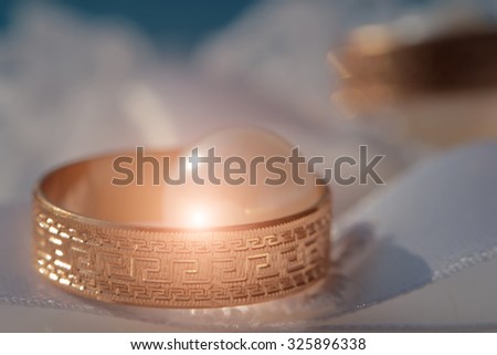 Closeup of two beautiful luxury golden engagement rings lying together on soft white fabric with lace and pearl beads on wedding celebration indoor with light splash, horizontal picture