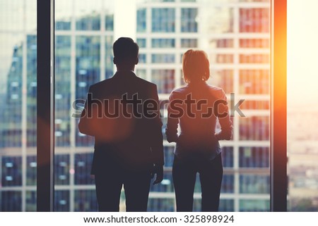 Back view silhouettes of two business partners looking thoughtfully out of a office window in situation of bankruptcy,team of businesspeople in fear or risk watching cityscape from skyscraper interior Royalty-Free Stock Photo #325898924