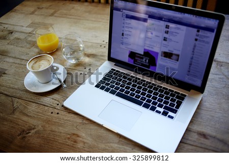 Cropped image of open net-book with screen for information content or advertising text message, there is portable laptop computer, cup of coffee and glass of juice on wooden table in cafe interior