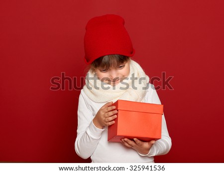 winter, child,  christmas holiday concept - happy girl in hat with box gift on red background