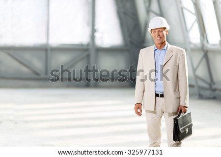 Real professional. Pleasant smiling cheerful delighted architect holding case and wearing helmet while working